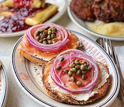 Bagel with cream cheese, lox, onion and capers on a Mamaleh's plate with other Jewish food.